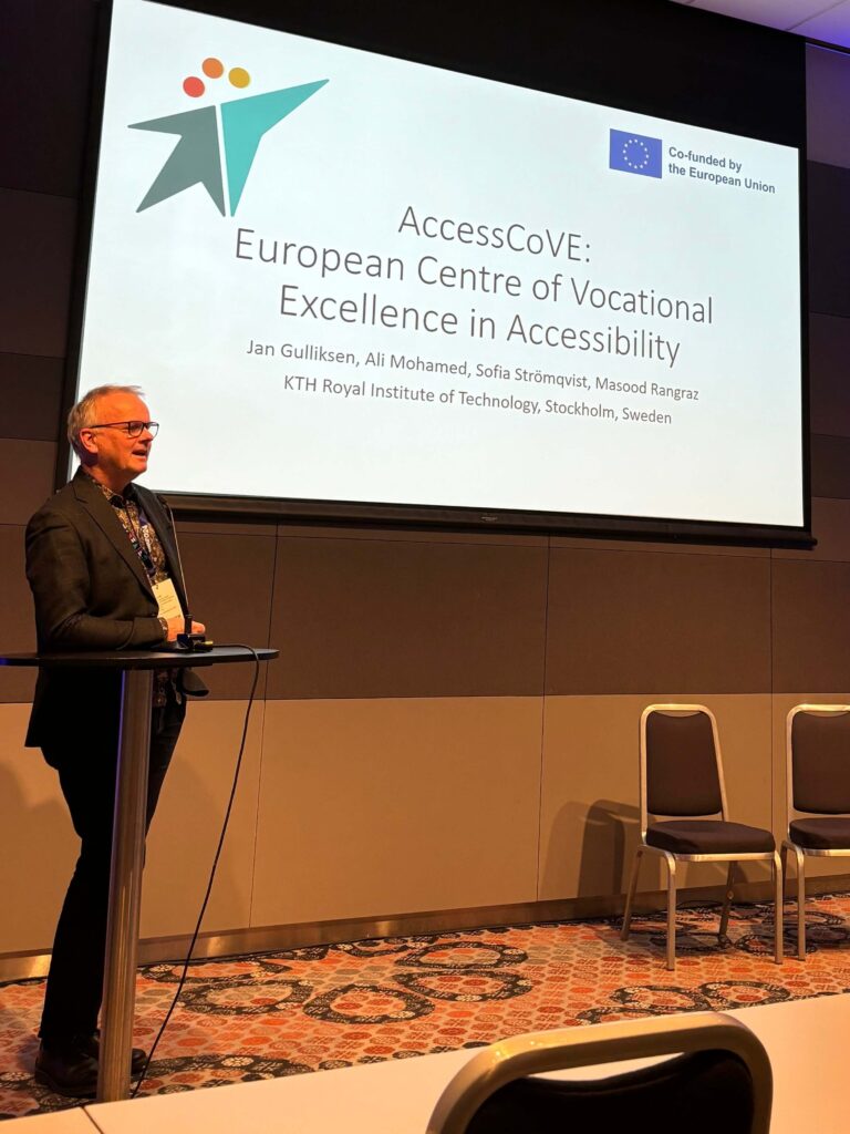 Jan Gulliksen stands facing an audience, preparing to present. A screen behind him displays the first slide of his presentation with the title of the AccessCoVE project.