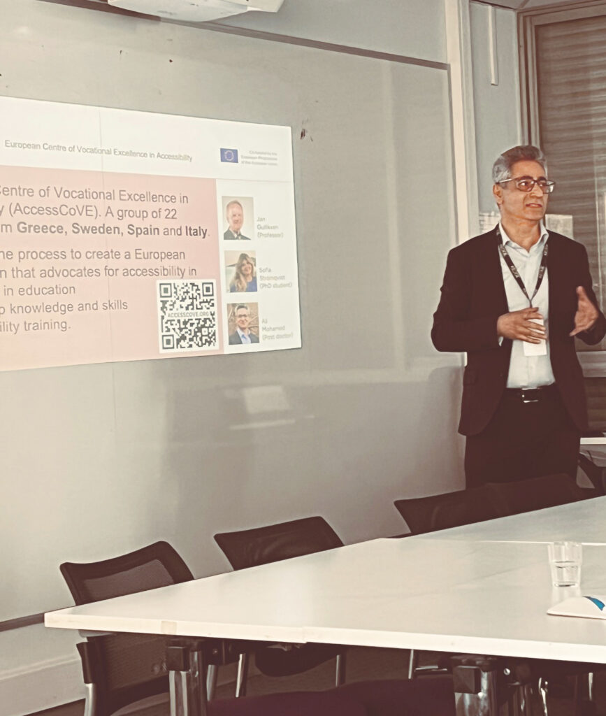Ali Mohamed, forskare vid KTH, står och talar i ett klassrumsliknande rum. Han håller en presentation om AccessCoVE-projektet. Bakom honom projiceras en presentationsbild på väggen. Bilden visar AccessCoVE:s logotyp, text om projektet, en QR-kod och foton på teammedlemmar från KTH.
